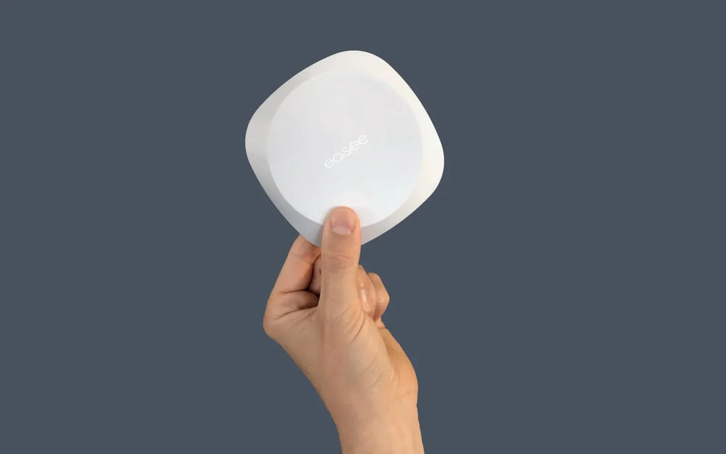 Hand holding small white Easee Equalizer wireless load balancer against slate-blue background showing palm-sized form factor